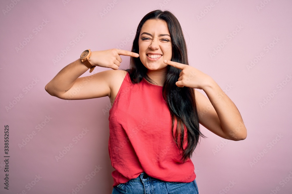 Young brunette woman wearing casual summer shirt over pink isolated background smiling cheerful showing and pointing with fingers teeth and mouth. Dental health concept. Young brunette woman wearing casual summer shirt over pink isolated background smiling cheerful showing and pointing with fingers teeth and mouth. Dental health concept.