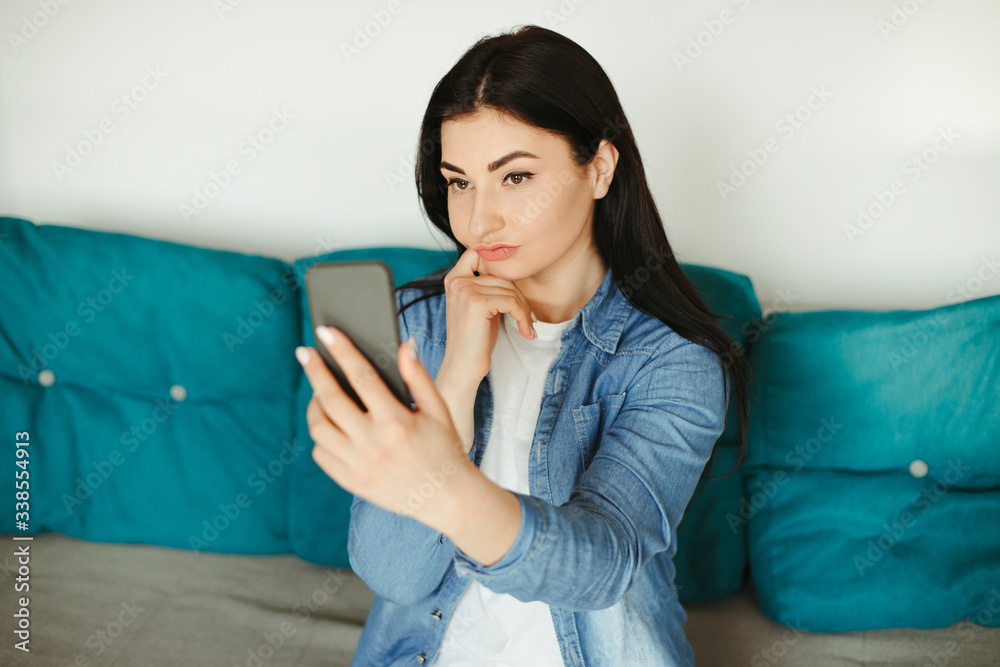 Woman taking a selfie with a smart phone in cozy room. Conversation, blogging and sharing impressions Woman taking a selfie with a smart phone in cozy room. Conversation, blogging and sharing impressions