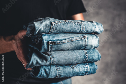 close up stack of folded denim blue jeans in hand over gray wall background, copy space