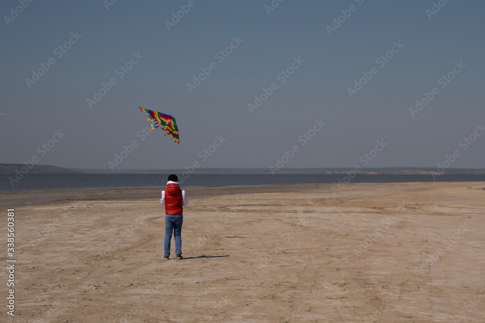 Obraz premium A 10 year old boy in a white sweatshirt and orange vest launches a kite on a deserted beach in solitude.