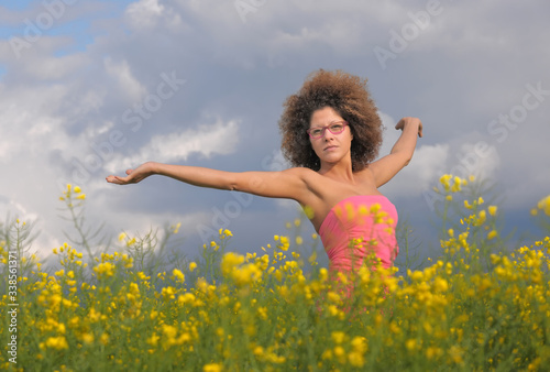 An attractíve young woman stands in a rapeseed field in springtime. She has a pink top on and wears trendy pink glasses. © Brigitte