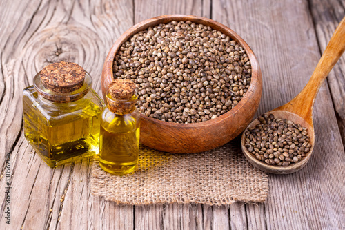 Heap of dried organic hemp seeds or cannabis plant seeds in spoon with glass of hemp seed oil on wooden backdrop. cannabis herb concept. hemp seed used birdseed