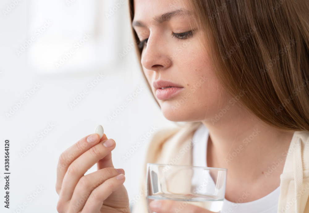 Headshot of young woman holding pill in one hand and glass of water in another, getting ready to take contraceptive, willing to protect herself from undesired pregnancy Headshot of young woman holding pill in one hand and glass of water in another, getting ready to take contraceptive, willing to protect herself from undesired pregnancy