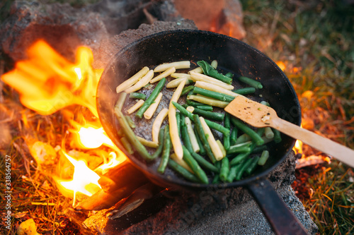 String beans in a pan. Cooking vegetables on an open fire. Food on a camping trip. Wooden spatula in a pan.