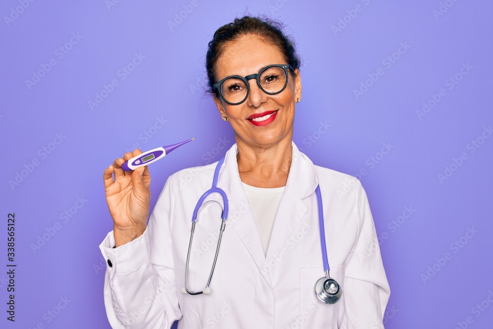 Middle age senior professional doctor woman holding medical thermometer with a happy face standing and smiling with a confident smile showing teeth Middle age senior professional doctor woman holding medical thermometer with a happy face standing and smiling with a confident smile showing teeth