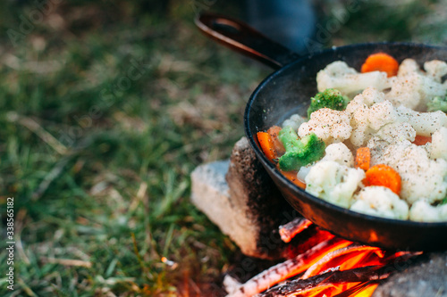 Cauliflower, broccoli and carrot in a pan. Cooking on an open fire. Outdoor food. Grilled vegetables. Food on a camping trip.