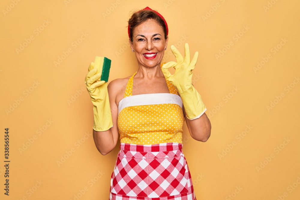 Middle age senior housewife pin up woman wearing 50s style retro dress using cleaner scrub doing ok sign with fingers, excellent symbol Middle age senior housewife pin up woman wearing 50s style retro dress using cleaner scrub doing ok sign with fingers, excellent symbol