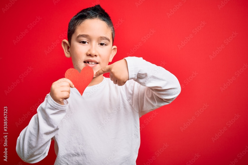 Young little boy kid holding heart paper shape over isolated red background very happy pointing with hand and finger Young little boy kid holding heart paper shape over isolated red background very happy pointing with hand and finger