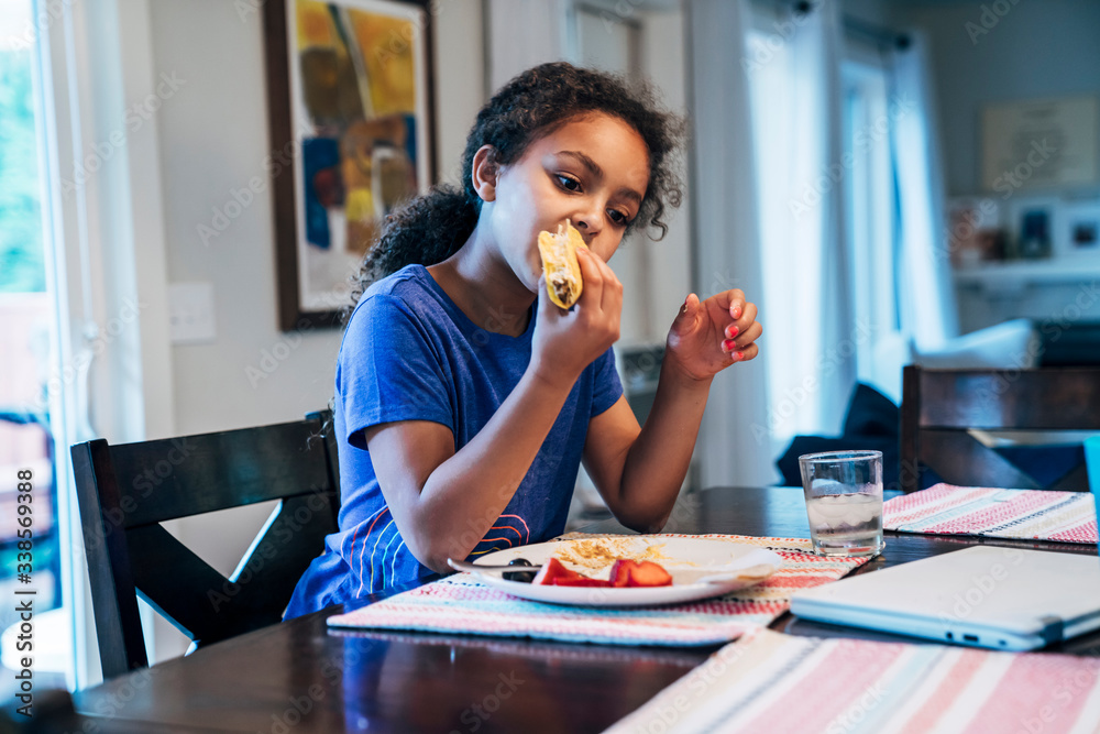 Girl eating tacos at dining room table in home Girl eating tacos at dining room table in home