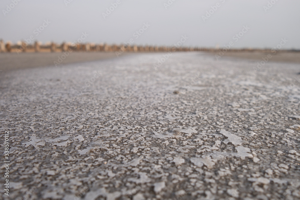 Sandy bottom of a dried reservoir with cracks and salt crystals.