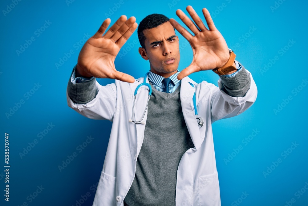 Handsome african american doctor man wearing coat and stethoscope over blue background doing frame using hands palms and fingers, camera perspective Handsome african american doctor man wearing coat and stethoscope over blue background doing frame using hands palms and fingers, camera perspective