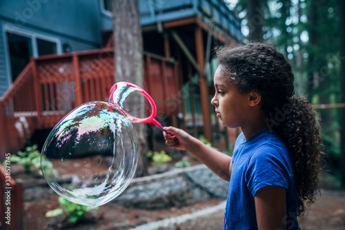 Girl blowing giant bubbles in the back yard of house