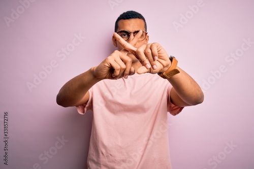 Handsome african american man wearing casual t-shirt and glasses over pink background Rejection expression crossing fingers doing negative sign