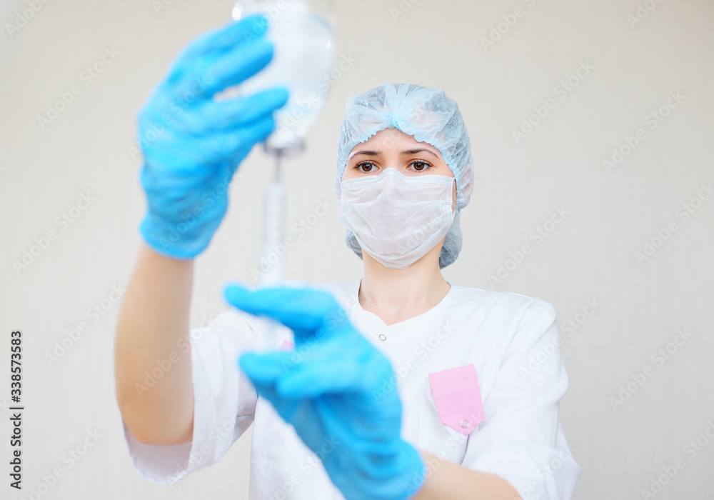a female doctor or nurse in a medical mask and rubber gloves prepares the injection. Saline solution of sodium chloride. Isotonic solution. a female doctor or nurse in a medical mask and rubber gloves prepares the injection. Saline solution of sodium chloride. Isotonic solution.