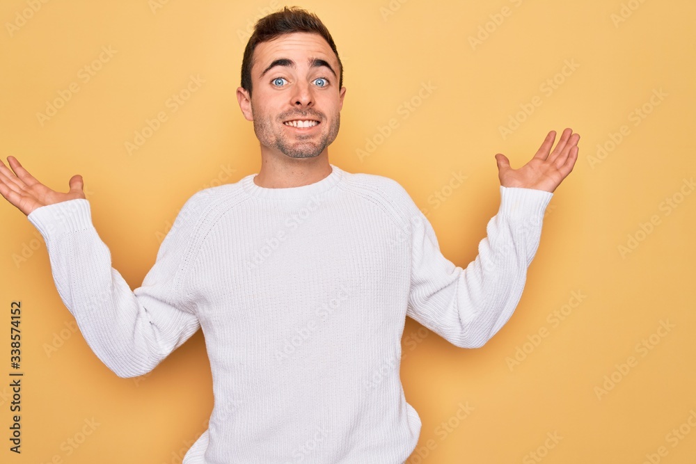 Young handsome man with blue eyes wearing casual sweater standing over yellow background smiling showing both hands open palms, presenting and advertising comparison and balance Young handsome man with blue eyes wearing casual sweater standing over yellow background smiling showing both hands open palms, presenting and advertising comparison and balance