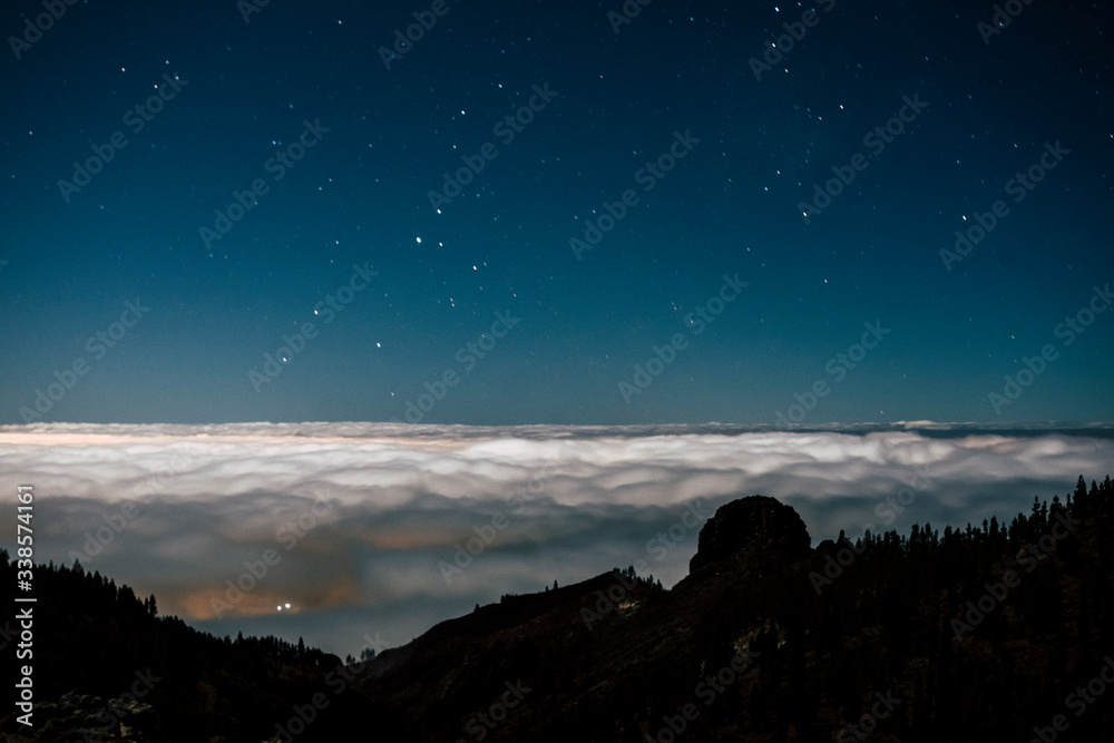 Night view of beautiful blue landscape with mountains in silhouette and night light in the sky with stars and white clouds in background