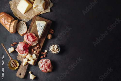 Tasting prosciutto and cheese platter with parmesan, dorblu, almonds, nuts, bread and honey on a wooden board on a dark background. Appetizer, aperitif, snack table. Top view. Space for text