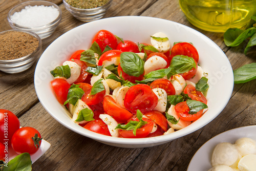 Traditional caprese salad on a rustic wooden table with ingredients. Selected focus.