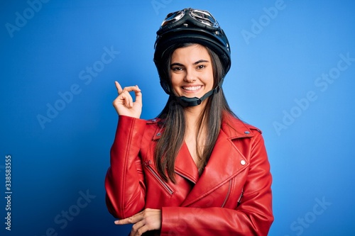 Young beautiful brunette motorcycliste woman wearing motorcycle helmet and jacket with a big smile on face, pointing with hand and finger to the side looking at the camera. © Krakenimages.com