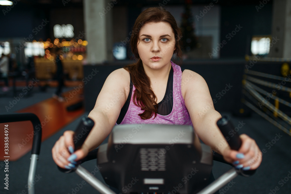 Overweight woman trains on exercise bike in gym Overweight woman trains on exercise bike in gym