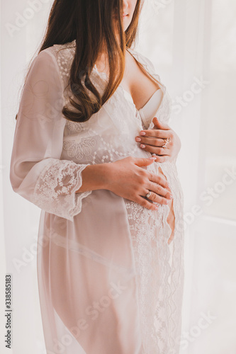 Young, pregnant woman posing in a white negligee dress.