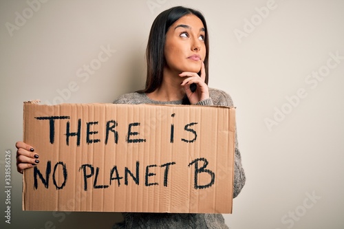 Young beautiful brunette activist woman protesting for save the planet holding banner serious face thinking about question, very confused idea © Krakenimages.com