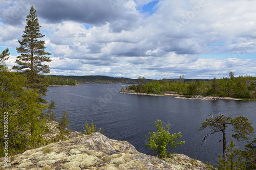 From the top of the island overlooks the skerries of Lake Ladoga. A rocky ledge, shrubbery and trees are visible in the foreground. In the background are visible islands and the channel of the lake.