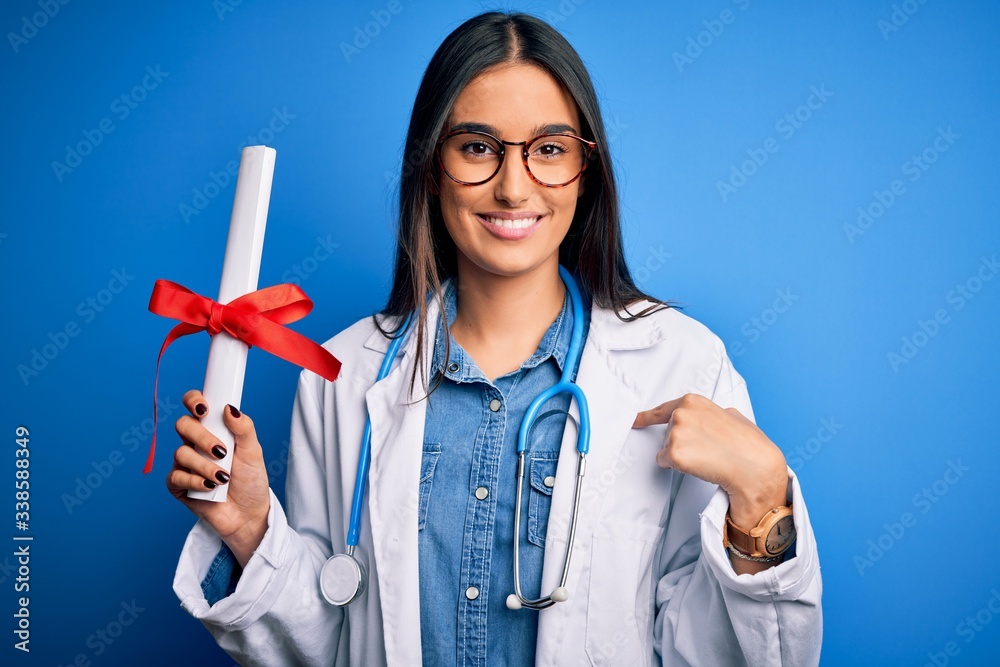 Young beautiful brunette doctor woman wearing glasses and coat holding diploma degree with surprise face pointing finger to himself Young beautiful brunette doctor woman wearing glasses and coat holding diploma degree with surprise face pointing finger to himself