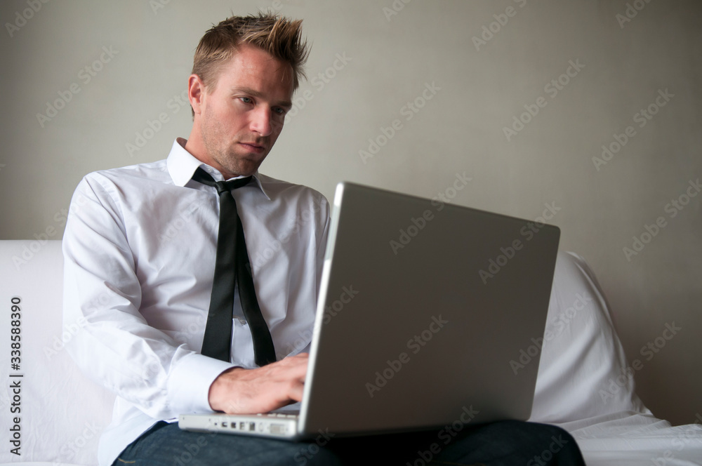 Man in stylish outfit sitting at home on the sofa browsing his laptop computer Man in stylish outfit sitting at home on the sofa browsing his laptop computer