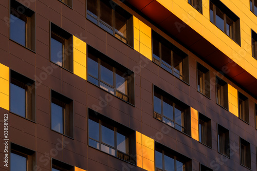 Fragment of a new elite residential building or commercial complex. Part of urban real estate. Yellow-brown modern ventilated facade with windows.