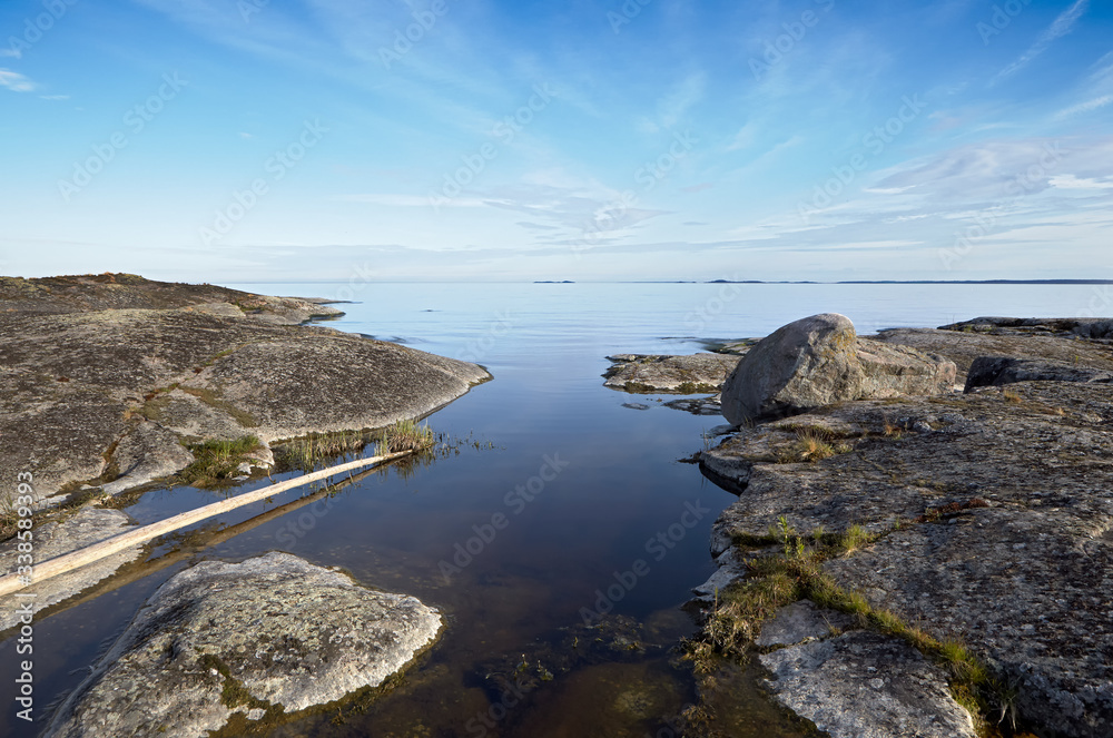 Landscape. Summer. Lake Ladoga. A narrow channel runs deep into the island. Calm water. Blue sky with clouds.