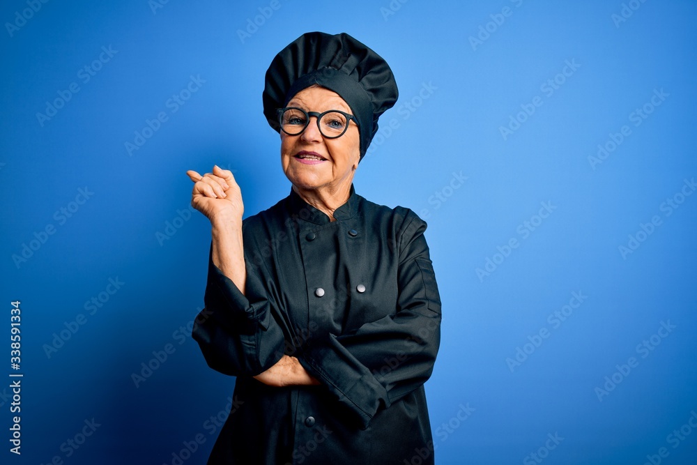 Senior beautiful grey-haired chef woman wearing cooker uniform and hat over blue background with a big smile on face, pointing with hand and finger to the side looking at the camera. Senior beautiful grey-haired chef woman wearing cooker uniform and hat over blue background with a big smile on face, pointing with hand and finger to the side looking at the camera.