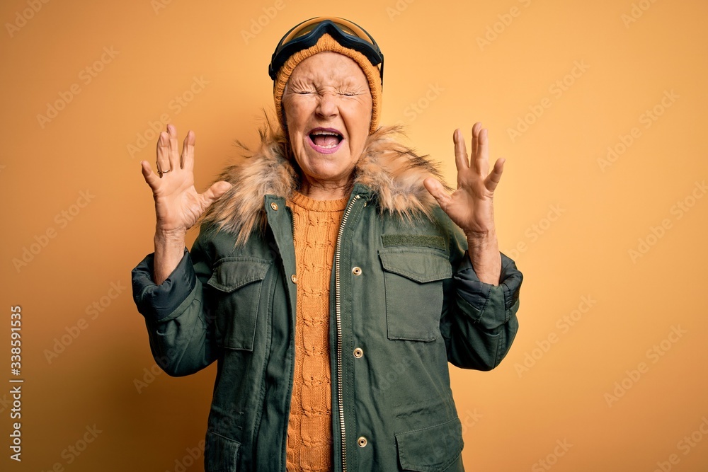 Senior beautiful grey-haired skier woman wearing snow sportswear and ski goggles celebrating mad and crazy for success with arms raised and closed eyes screaming excited. Winner concept Senior beautiful grey-haired skier woman wearing snow sportswear and ski goggles celebrating mad and crazy for success with arms raised and closed eyes screaming excited. Winner concept