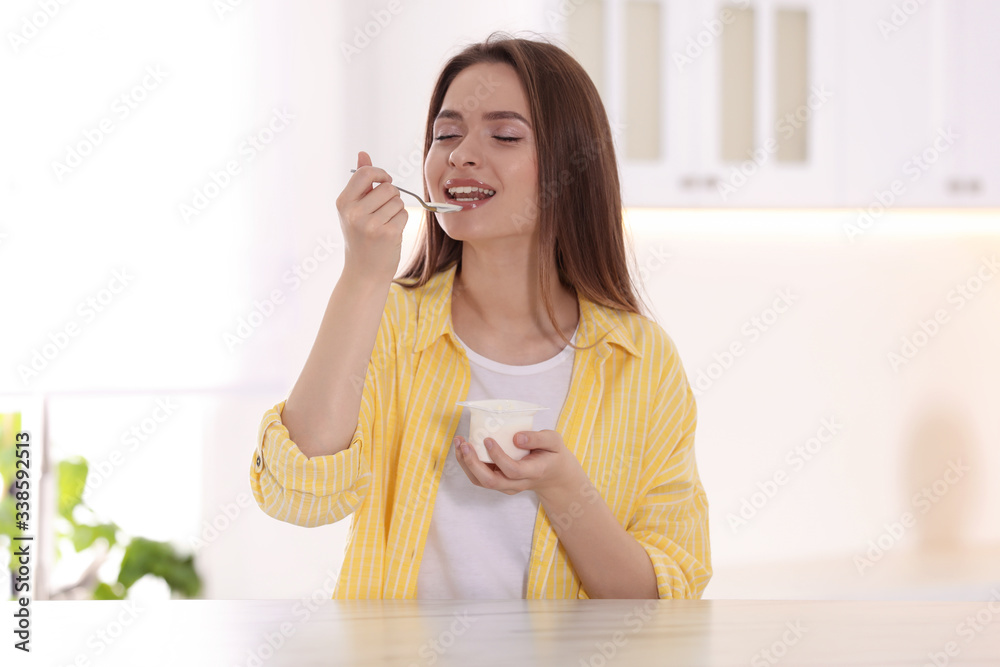Young attractive woman eating tasty yogurt at table in kitchen Young attractive woman eating tasty yogurt at table in kitchen
