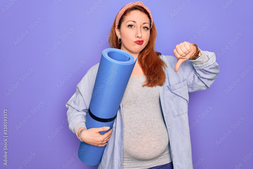 Young beautiful redhead pregnant woman expecting baby holding mat to do prenatal exercise with angry face, negative sign showing dislike with thumbs down, rejection concept Young beautiful redhead pregnant woman expecting baby holding mat to do prenatal exercise with angry face, negative sign showing dislike with thumbs down, rejection concept