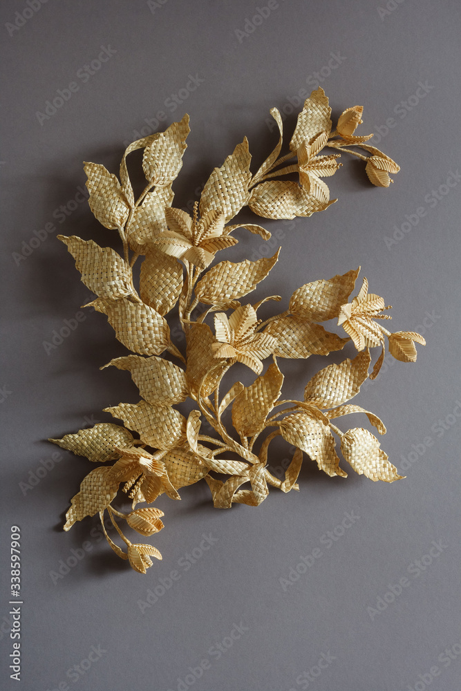 Branch with leaves and flowers is made of straw Straw wall decoration. The products are made of straw. Decoration of straw on a gray background. Branch with leaves and flowers is made of straw Straw wall decoration. The products are made of straw. Decoration of straw on a gray background.
