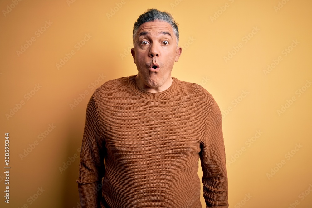Middle age handsome grey-haired man wearing casual sweater over yellow background afraid and shocked with surprise expression, fear and excited face. Middle age handsome grey-haired man wearing casual sweater over yellow background afraid and shocked with surprise expression, fear and excited face.