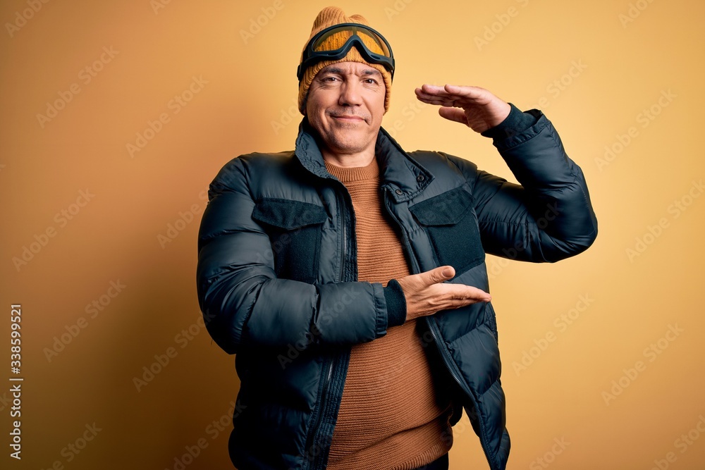 Middle age handsome grey-haired skier man on vacation wearing ski goggles gesturing with hands showing big and large size sign, measure symbol. Smiling looking at the camera. Measuring concept. Middle age handsome grey-haired skier man on vacation wearing ski goggles gesturing with hands showing big and large size sign, measure symbol. Smiling looking at the camera. Measuring concept.