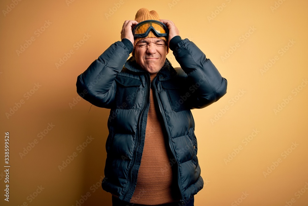 Middle age handsome grey-haired skier man on vacation wearing ski goggles suffering from headache desperate and stressed because pain and migraine. Hands on head. Middle age handsome grey-haired skier man on vacation wearing ski goggles suffering from headache desperate and stressed because pain and migraine. Hands on head.