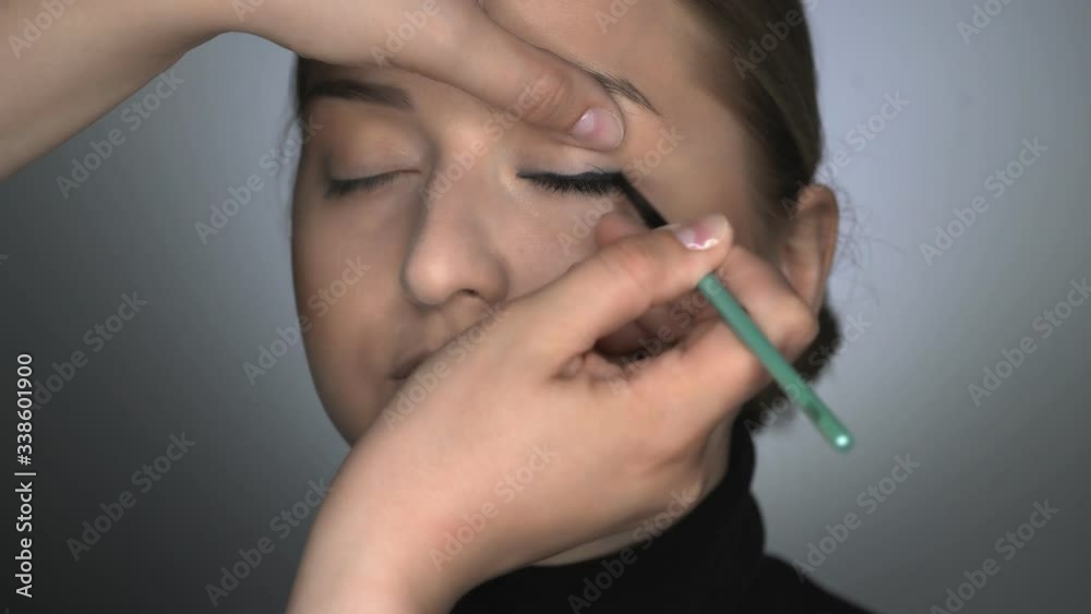 Makeup artist making professional make-up for young woman in beauty studio. Make up Artist applies black eyeliner to eyelid