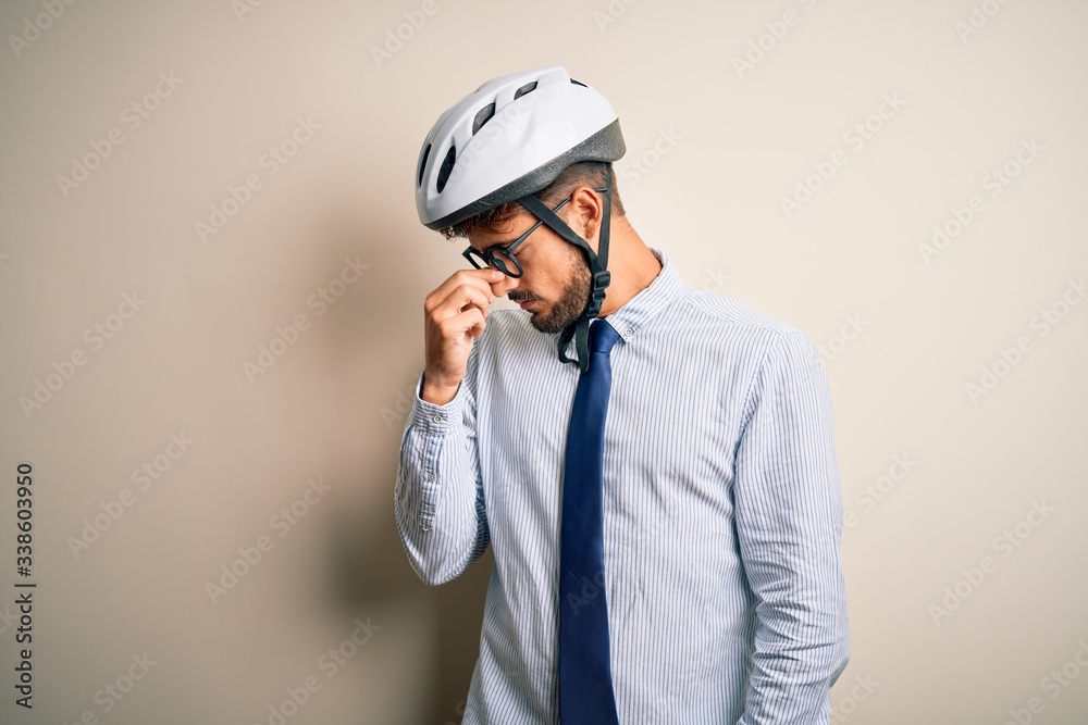 Young businessman wearing glasses and bike helmet standing over isolated white bakground tired rubbing nose and eyes feeling fatigue and headache. Stress and frustration concept.