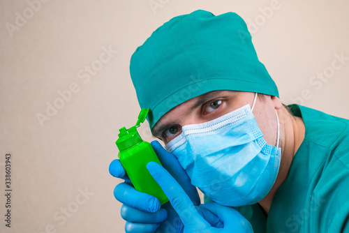 Doctor in green suit and blue mask gloves with green antiseptic bottle in hand on yellow background. photo