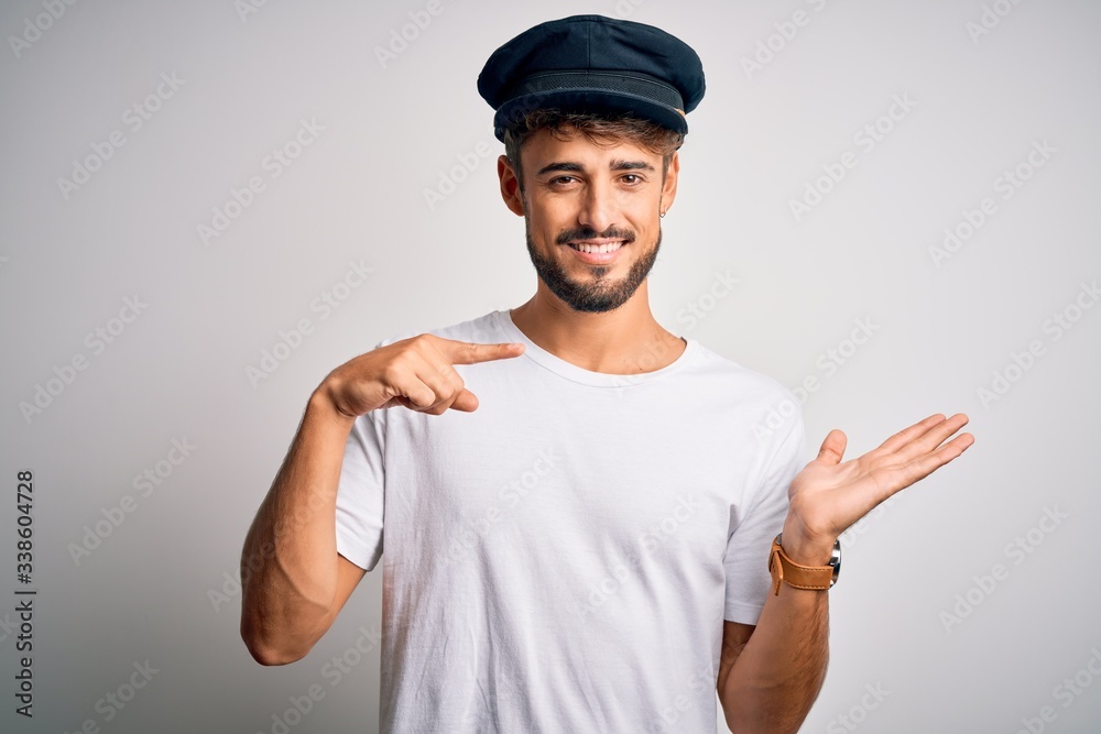 Young driver man with beard wearing hat standing over isolated white background amazed and smiling to the camera while presenting with hand and pointing with finger. Young driver man with beard wearing hat standing over isolated white background amazed and smiling to the camera while presenting with hand and pointing with finger.