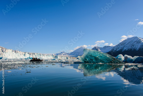 Big blue piece of ice in Arctic sea. Inflatable boat with tourists.