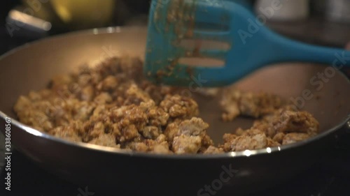 Closeup View Of Frying Ground Chicken In A Shallow Cooking Pan With A Blue Slotter Turner - Slow Motion photo