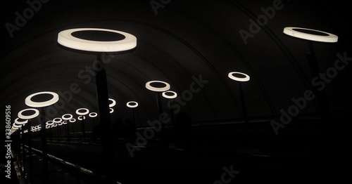 Black and white monochrome picture of modern metro station interior with lights in form of rings.