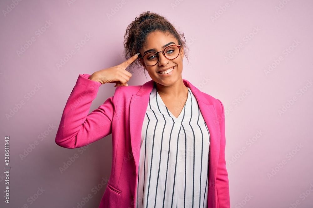 Beautiful african american businesswoman wearing jacket and glasses over pink background Smiling pointing to head with one finger, great idea or thought, good memory