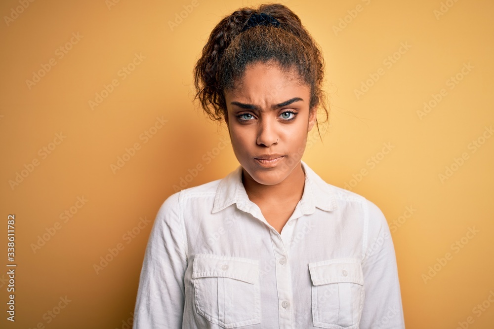 Young beautiful african american girl wearing casual shirt standing over yellow background skeptic and nervous, frowning upset because of problem. Negative person. Young beautiful african american girl wearing casual shirt standing over yellow background skeptic and nervous, frowning upset because of problem. Negative person.