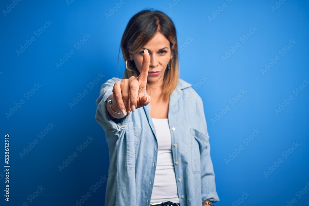 Middle age beautiful woman wearing casual shirt standing over isolated blue background Pointing with finger up and angry expression, showing no gesture Middle age beautiful woman wearing casual shirt standing over isolated blue background Pointing with finger up and angry expression, showing no gesture