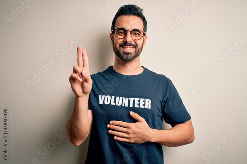 Handsome man with beard wearing t-shirt with volunteer message over white background smiling swearing with hand on chest and fingers up, making a loyalty promise oath © Krakenimages.com